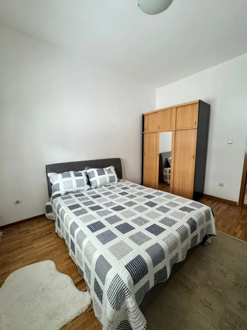 Namještena spavaća soba sa bračnim krevetom i drvenim ormarom.