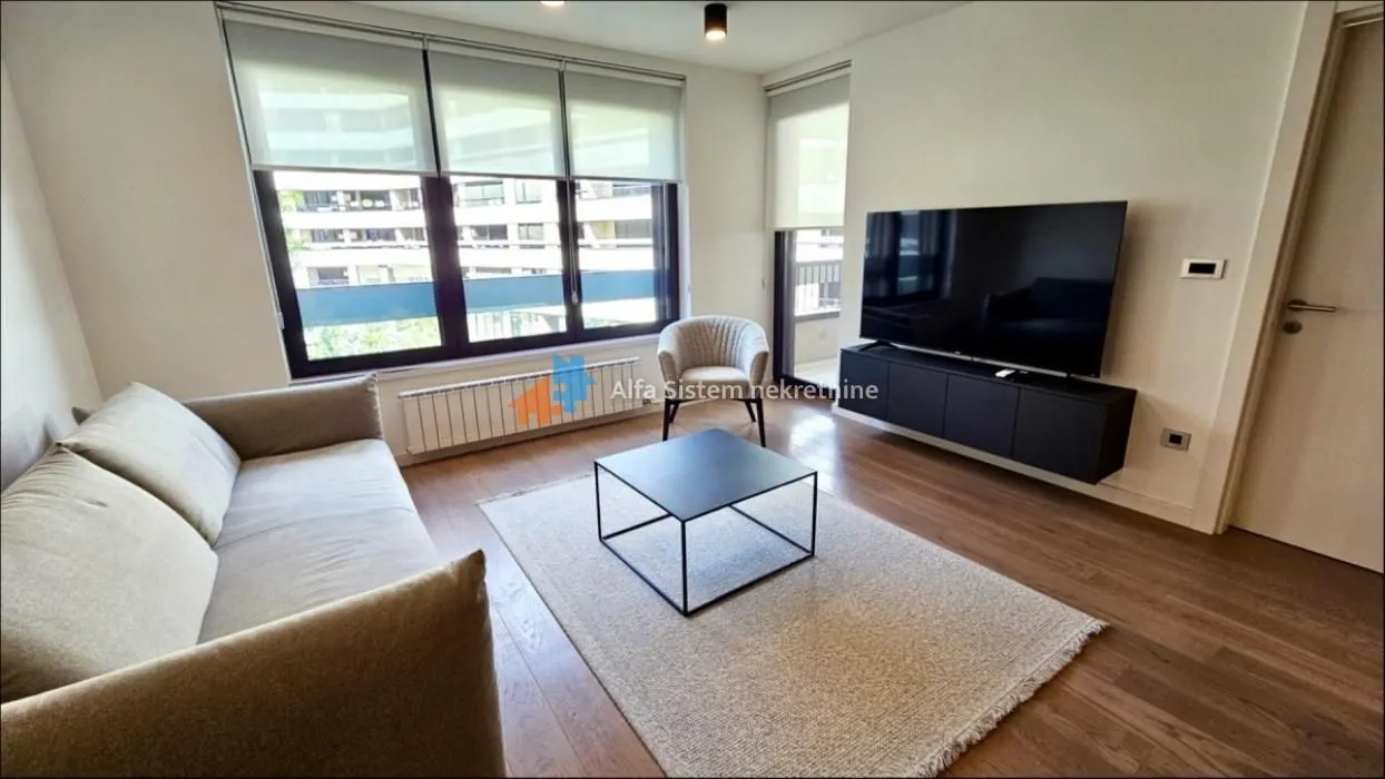 Dnevna soba sa garniturom, televizorom i velikim prozorima.