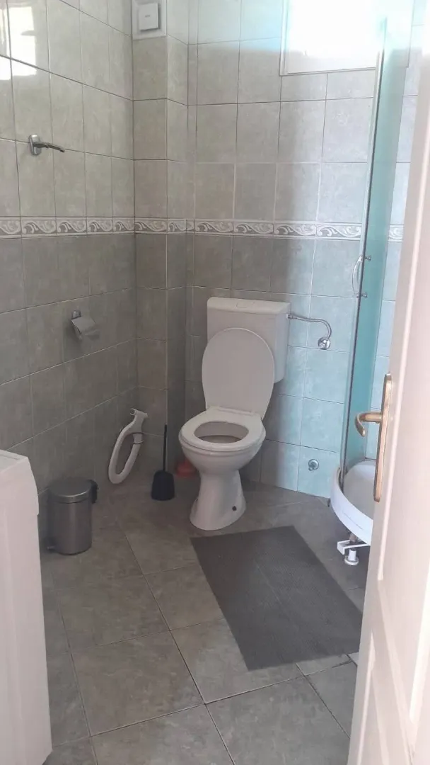 Manje kupatilo sa keramičkim pločicama, wc šoljom i tuš kabinom.