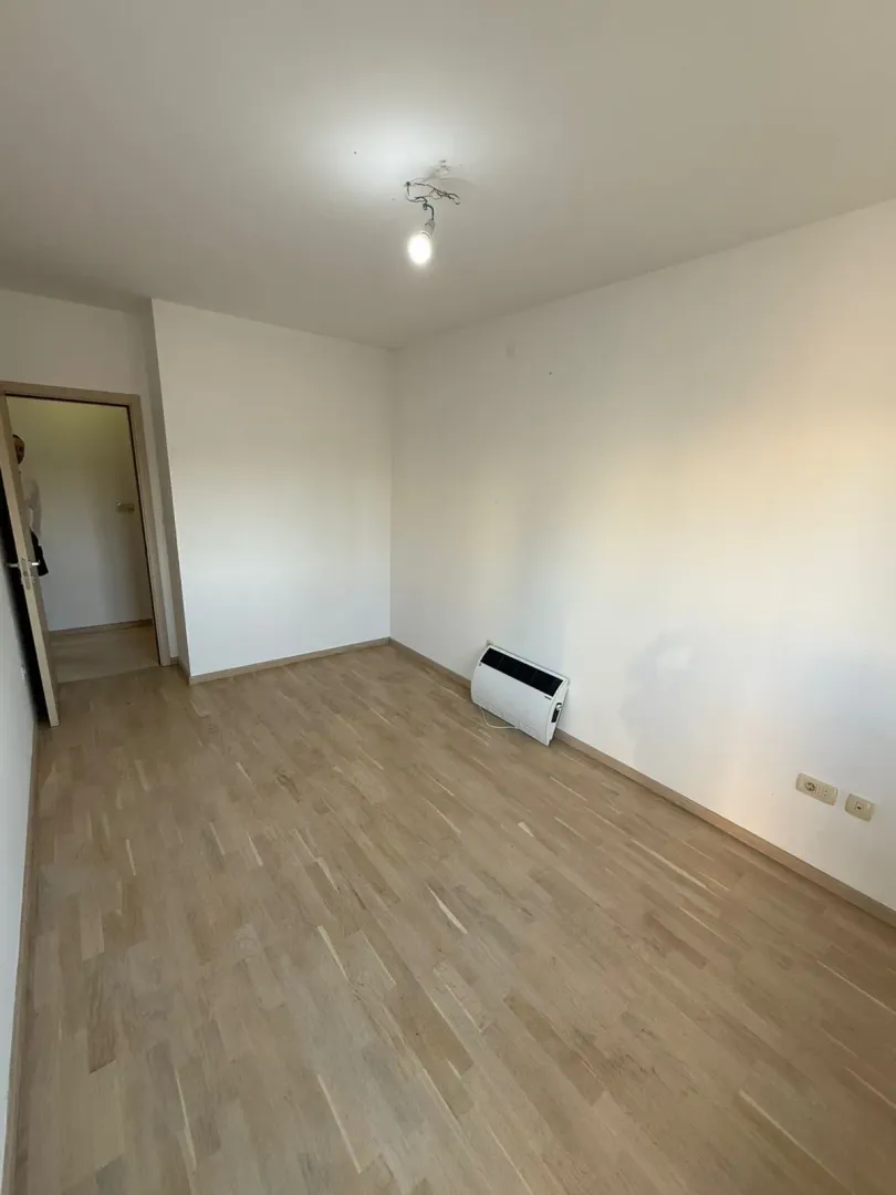 Prazna soba sa bijelim zidovima, parketom i klima uređajem.