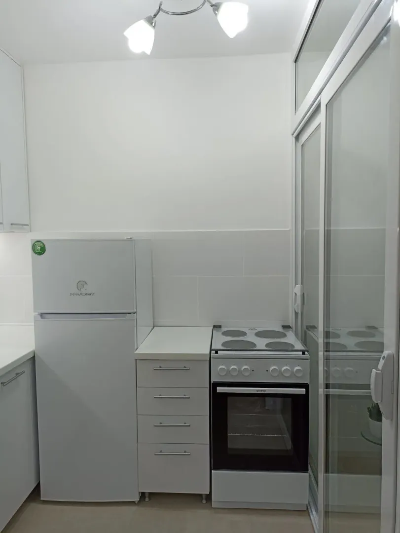 Manja bijela kuhinja sa frižiderom i šporetom.
