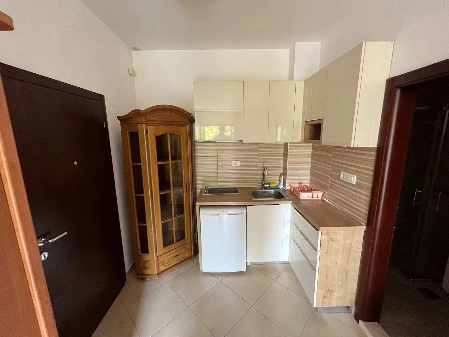 Small kitchen with light-colored cabinets and a wooden display cabinet.