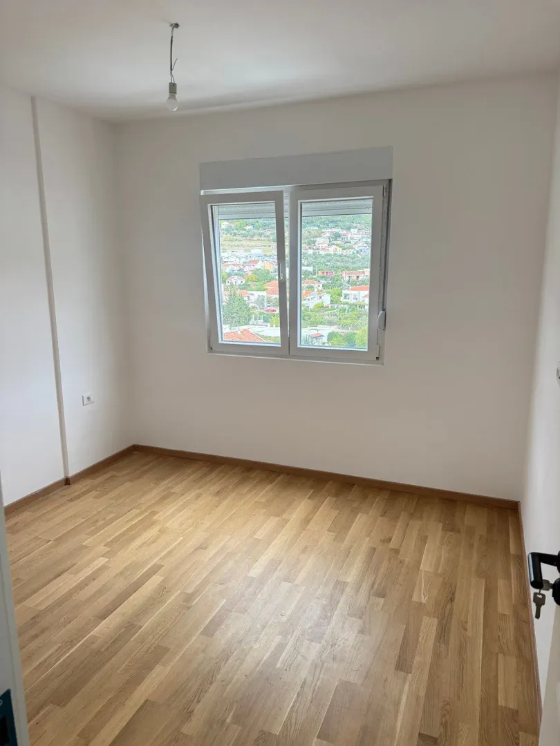 Empty room with white walls, parquet flooring, and a window view.