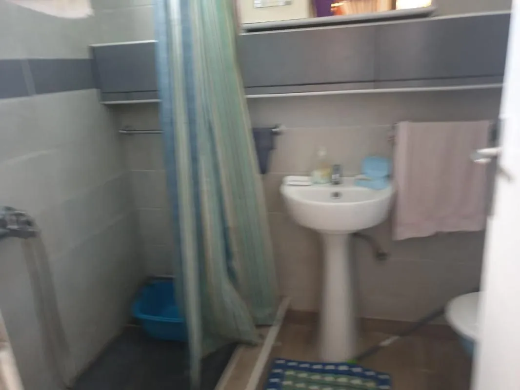 Manje kupatilo sa umivaonikom, tuš kabinom sa zavesom i zidnim elementima.