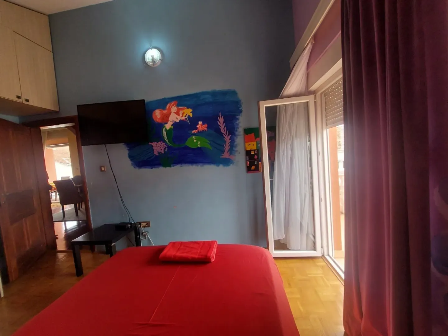 Spavaća soba sa crvenim krevetom i muralom na zidu.