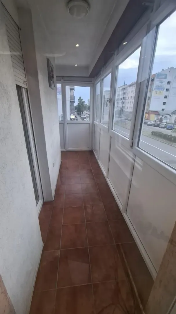 Zastakljeni balkon sa keramičkim pločicama na podu i pogledom na ulicu.