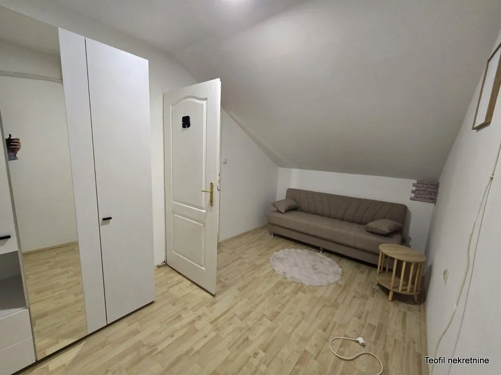 Manja soba sa kaučem, ormarom i laminatnim podom u potkrovlju.