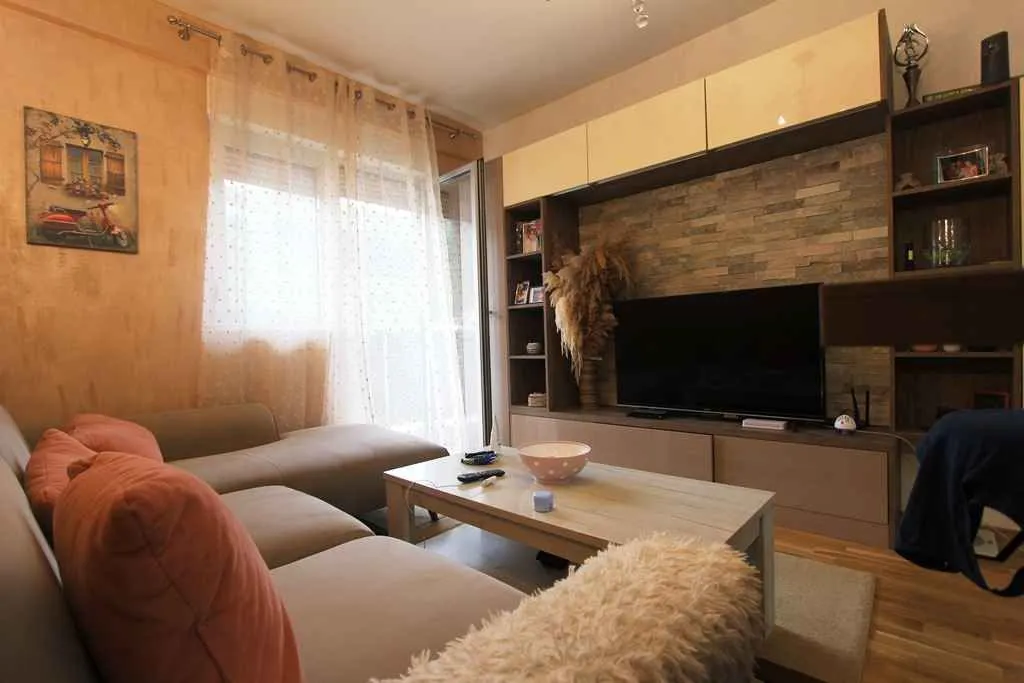 Dnevna soba sa garniturom, TV komodom i izlazom na terasu.