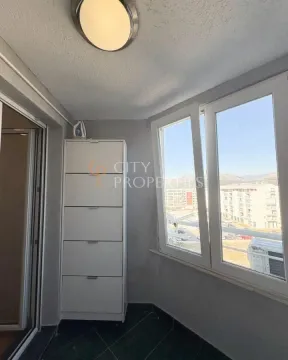 Zastakljeni balkon sa bijelim ormarićem i pogledom na grad. - image 2