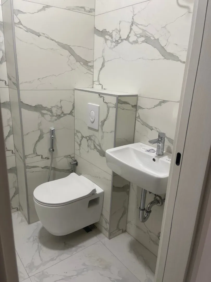 Small bathroom clad in marble-pattern tiles with a wall-hung toilet and a washbasin.