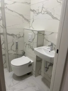 Small bathroom clad in marble-pattern tiles with a wall-hung toilet and a washbasin. - image 5