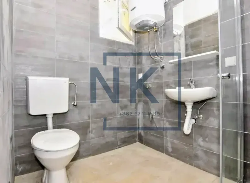 Bathroom tiled in gray with a toilet, washbasin, shower cabin, and water heater.