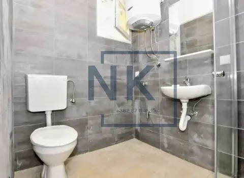 Bathroom tiled in gray with a toilet, washbasin, shower cabin, and water heater. - image 5