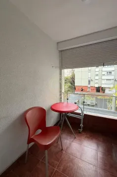 Manji zatvoreni balkon sa stočićem i crvenom stolicom i pogledom na zgrade. - image 15