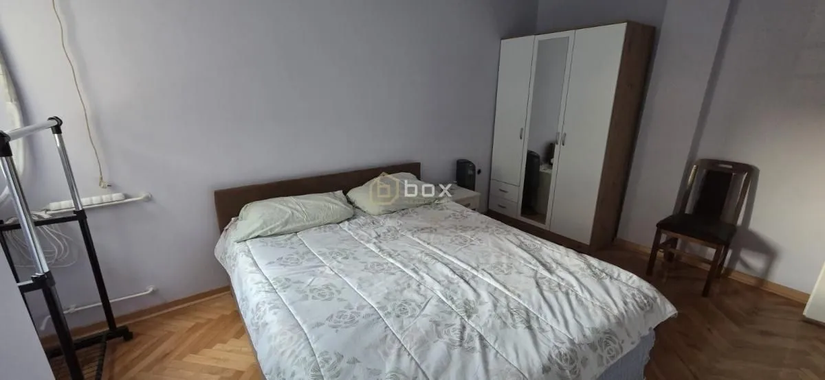 Spavaća soba sa bračnim krevetom, ormarom i drvenim podom.