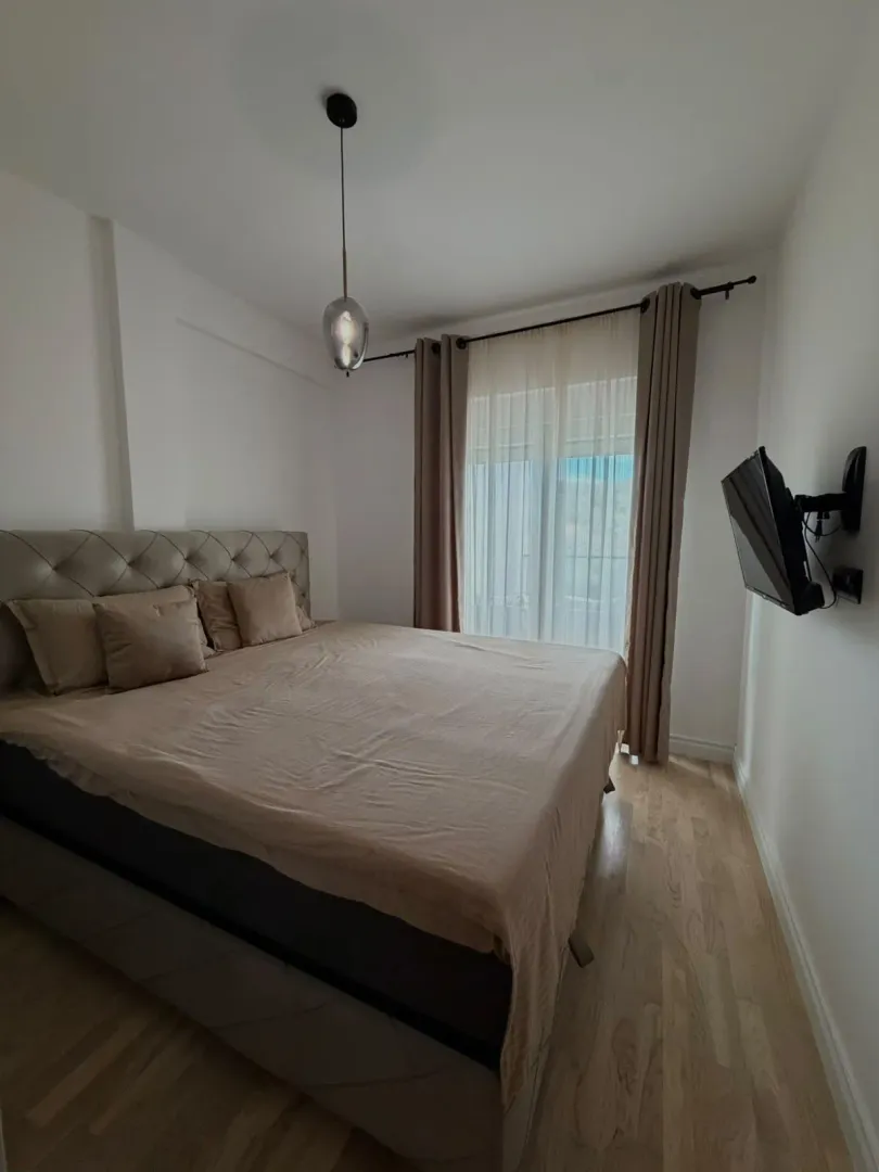 A furnished bedroom with a double bed and a window with light curtains.