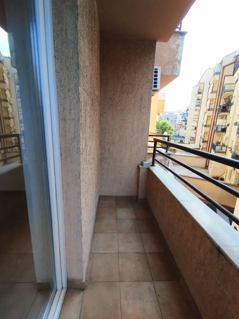 Nenamešten balkon sa pločicama i pogledom na okolne zgrade.