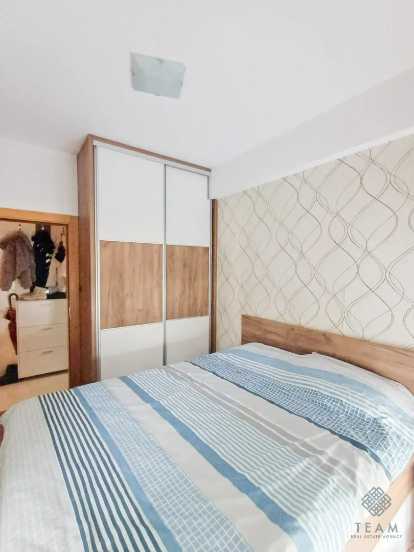 Furnished bedroom with a double bed, wardrobe, and patterned wallpaper on the wall.