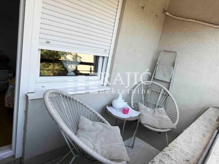 Small covered terrace with two chairs, a small table, and a window with blinds.