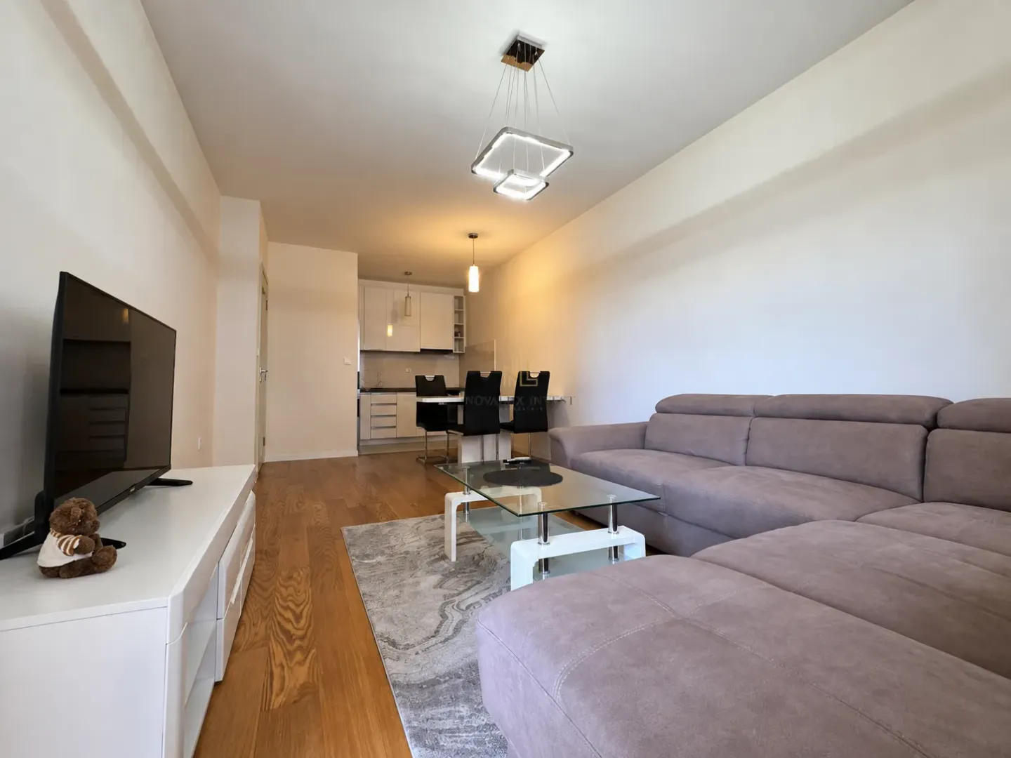 Living room with a sofa, TV, and dining area in the background.