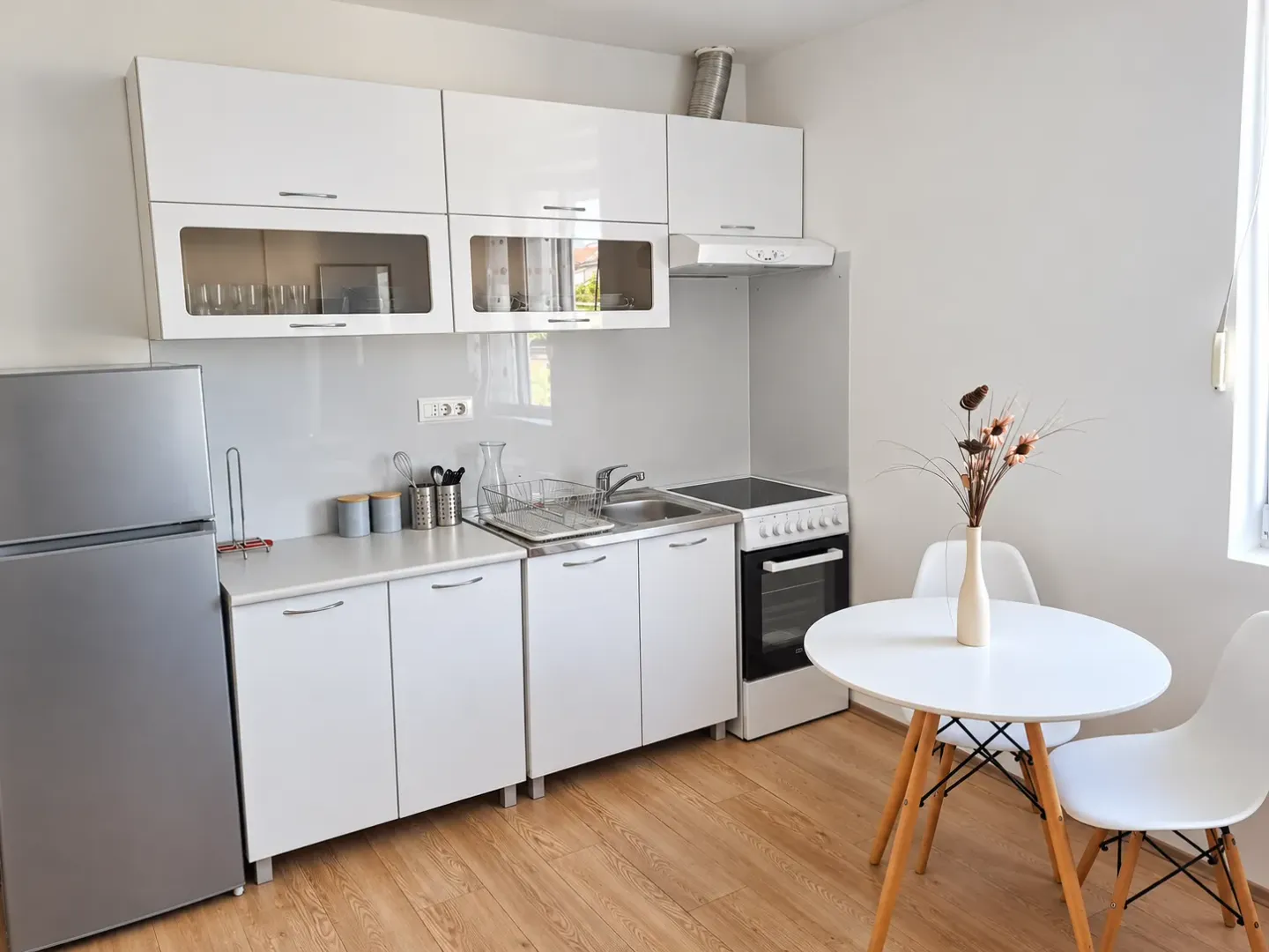 White kitchen with a refrigerator, stove, and a dining table with chairs.