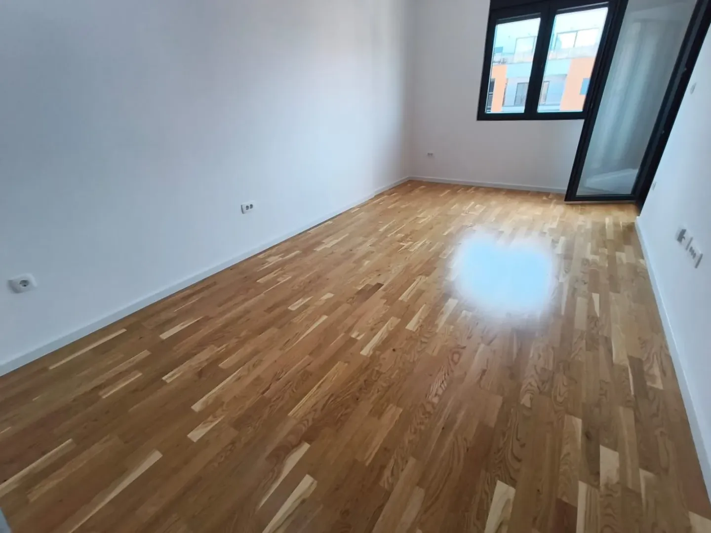 Prazna soba sa parketom i izlazom na terasu.