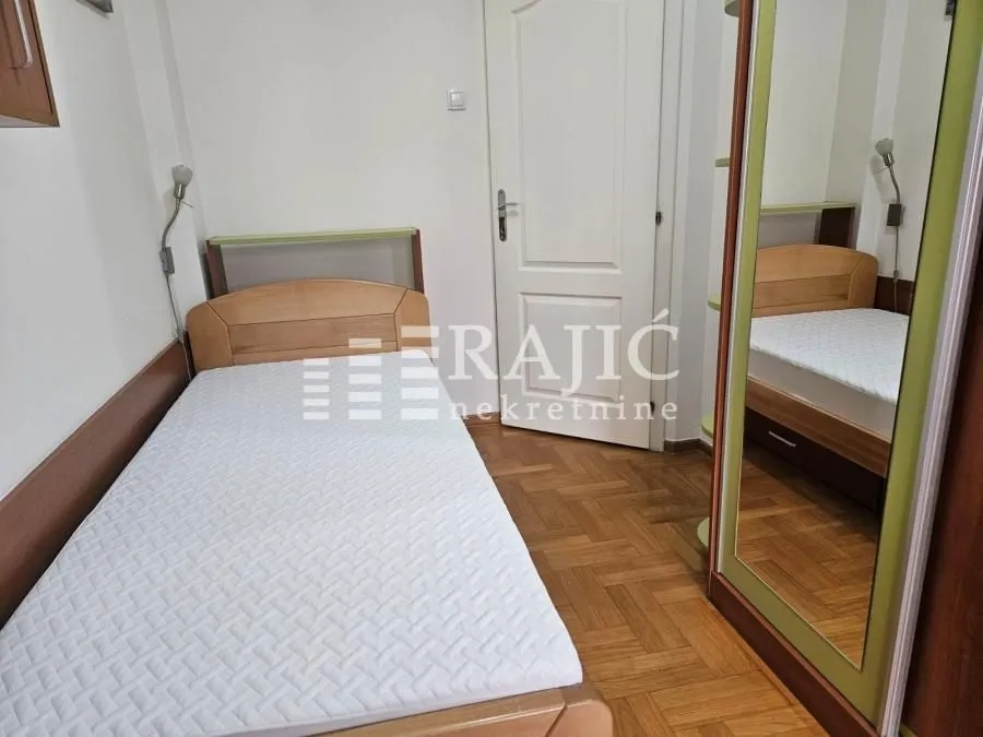 Smaller bedroom with a bed and a wooden wardrobe with a mirror.