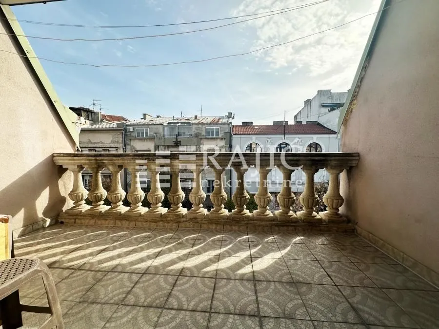 Covered balcony with a stone balustrade and a city view.