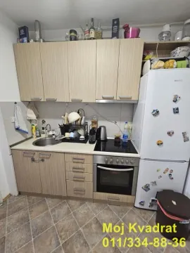 Manja kuhinja sa drvenim elementima, belim frižiderom i šporetom. - image 4