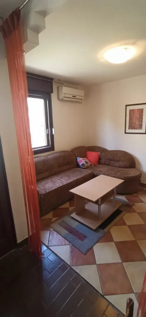 Dnevna soba sa ugaonom garniturom, klub stočićem i keramičkim pločicama na podu.
