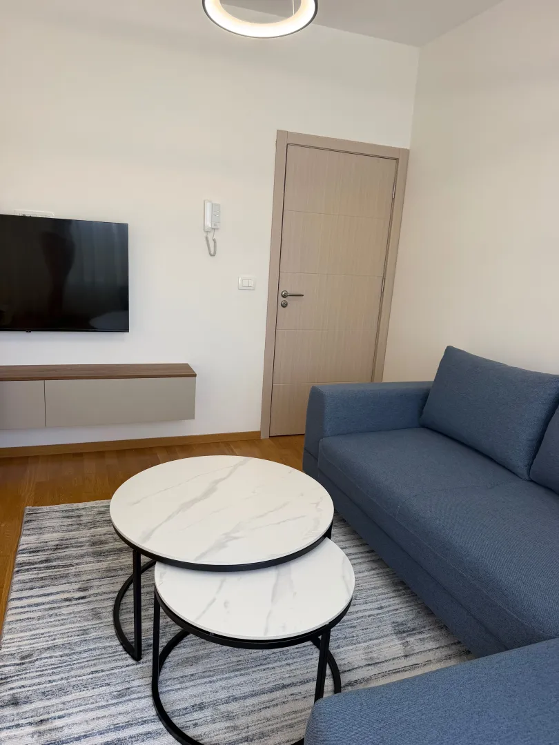 Dnevna soba sa plavom garniturom, okruglim stočićem i TV-om.