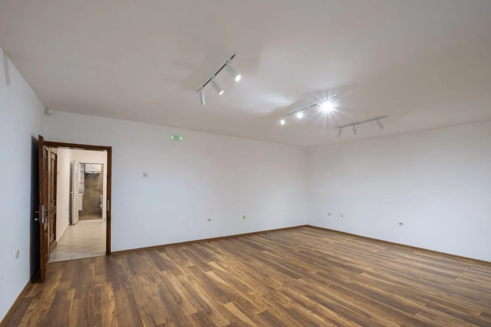 Empty room with white walls, wooden flooring, and ceiling lighting.