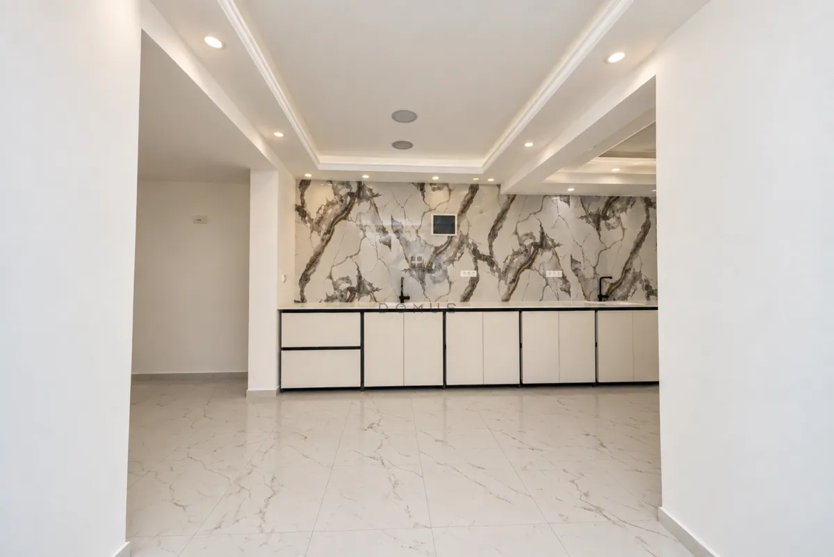 Modern kitchen with white cabinets and marble-look wall panel.