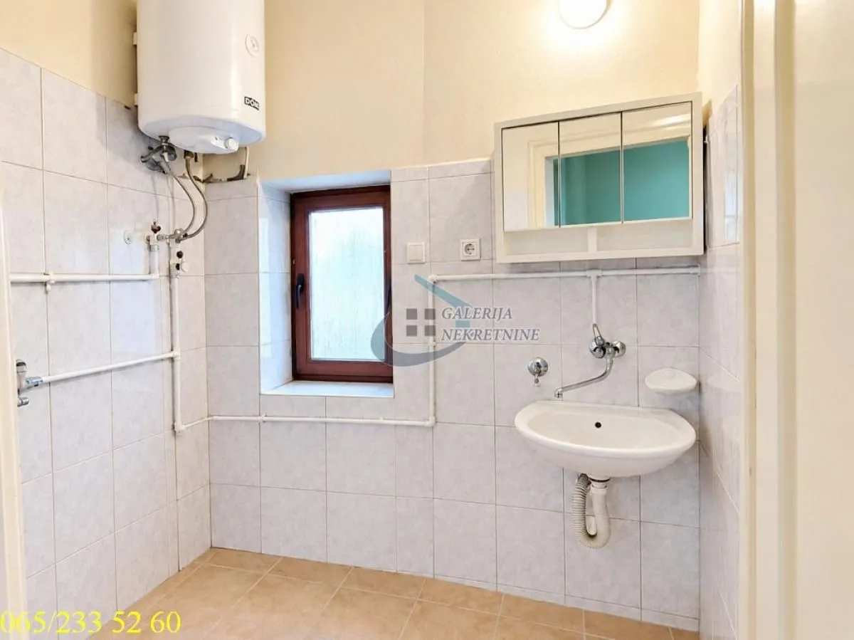 Manje kupatilo obloženo keramičkim pločicama sa umivaonikom i bojlerom.