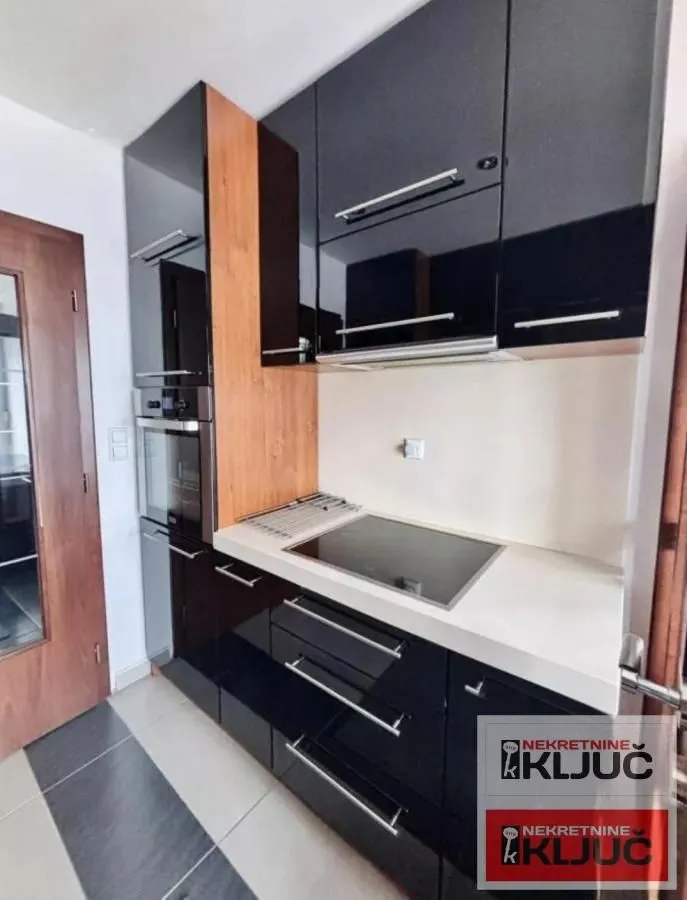 Moderna kuhinja sa crnim elementima i ugradnom rernom.