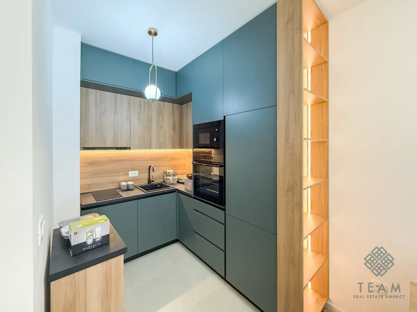 Modern kitchen with dark green cabinets and wooden details.