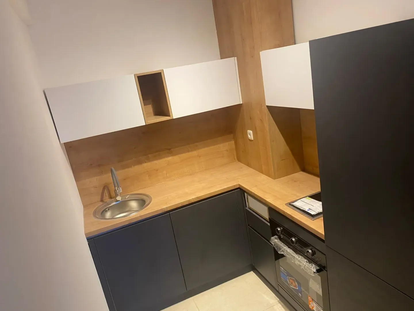 Moderna kuhinja sa tamnim elementima i drvenim detaljima.