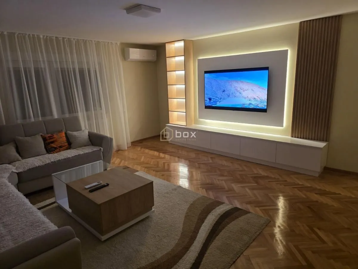 Dnevna soba sa garniturom, stočićem i TV-om sa pozadinskim osvetljenjem.