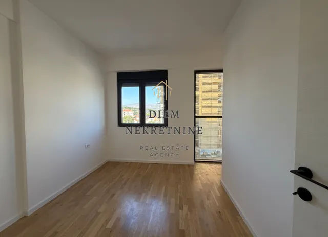Empty room with wooden flooring and windows.