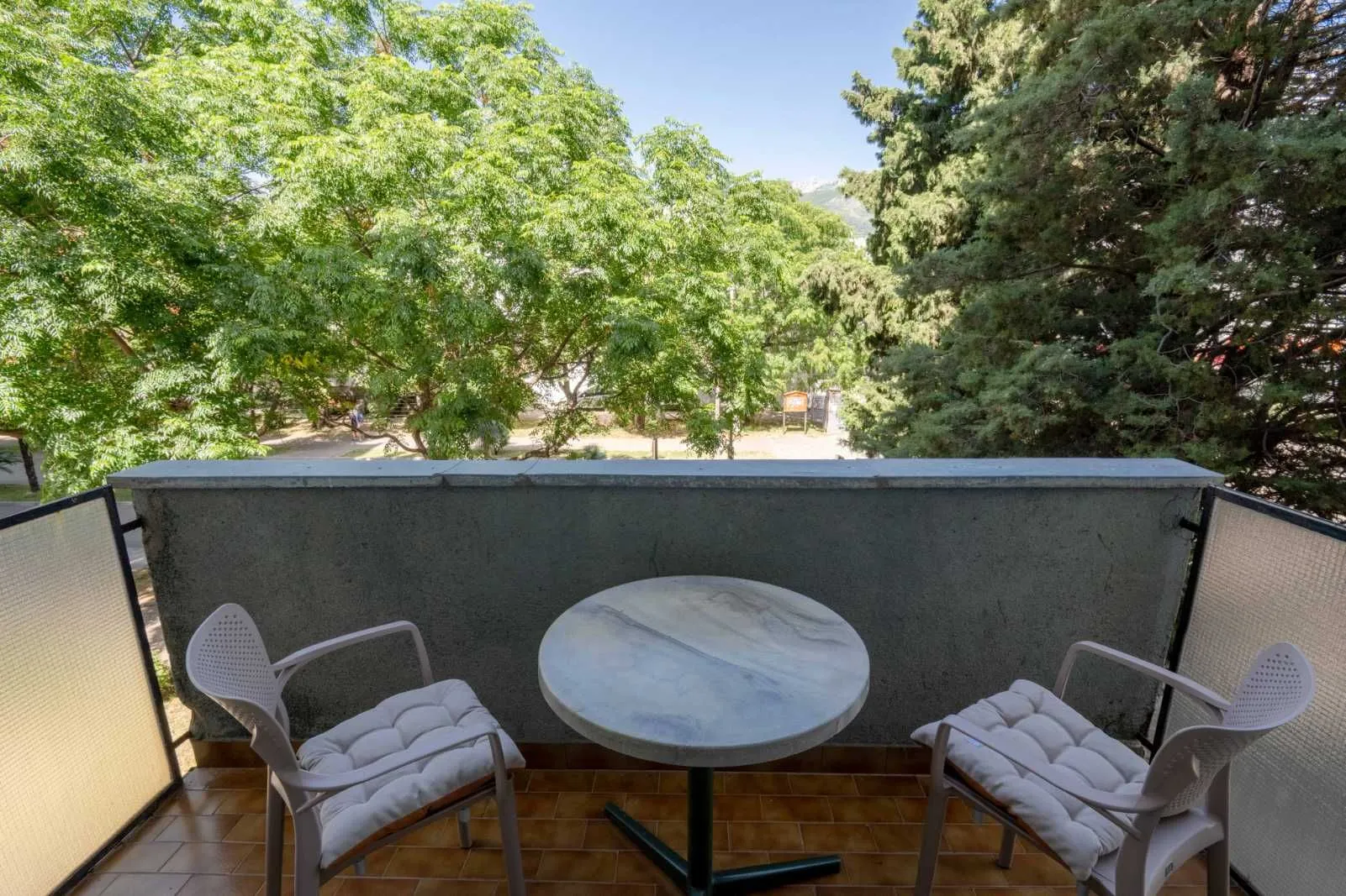 Furnished balcony with a table, chairs, and a view of greenery.