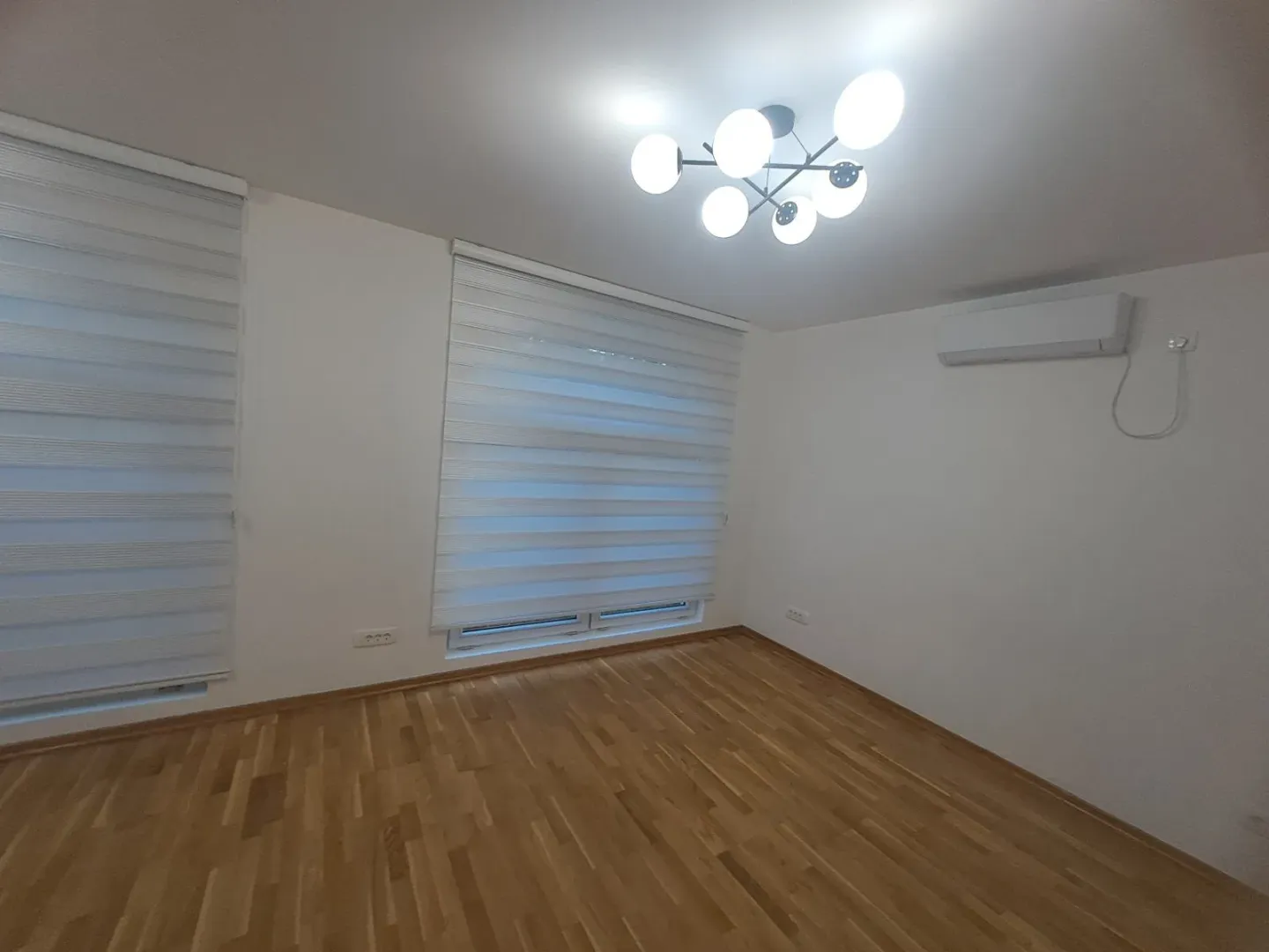 Empty room with hardwood flooring and an air conditioning unit on the wall.