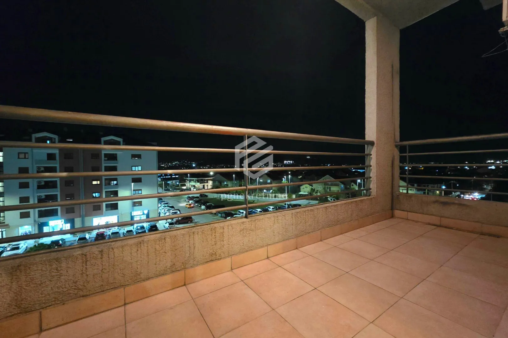 Unfurnished balcony with a view of the city at night and parking.