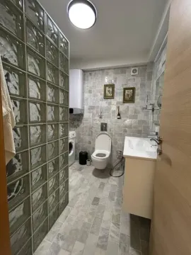 Kupatilo obloženo pločicama sa toaletom, umivaonikom i tuš kabinom od staklenih blokova. - image 4