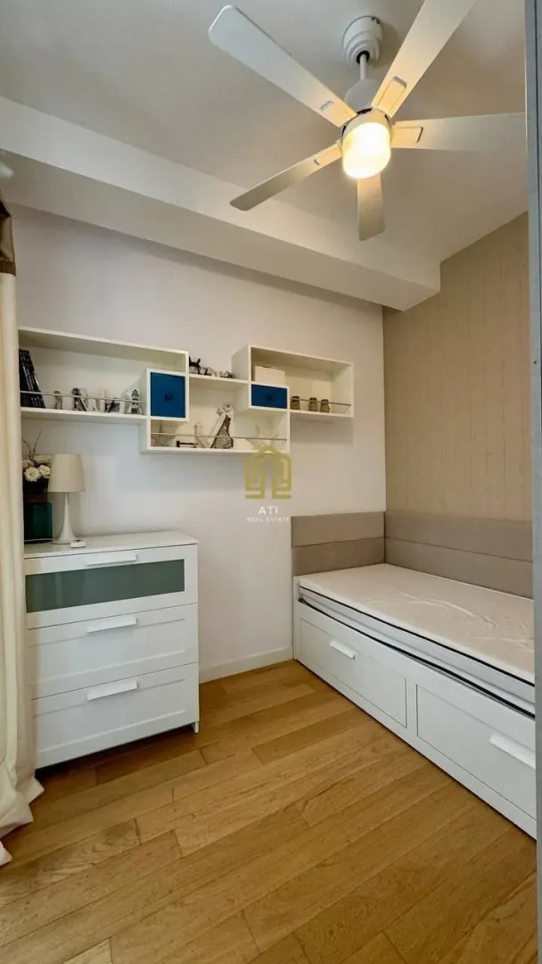 Small bedroom with a bed, dresser, and wall shelves.