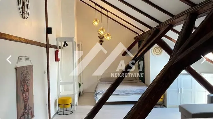 Potkrovlje sa spavaćom sobom i drvenim krovnim gredama.