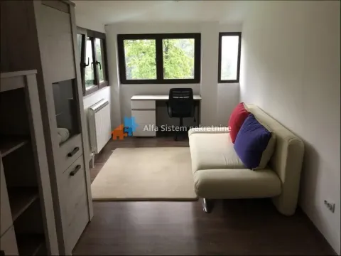 Living room with a sofa, desk, and windows overlooking greenery. - image 4