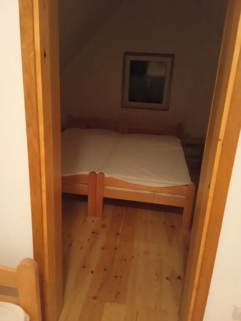 Jednostavna spavaća soba sa drvenim krevetom viđena kroz štok od vrata.