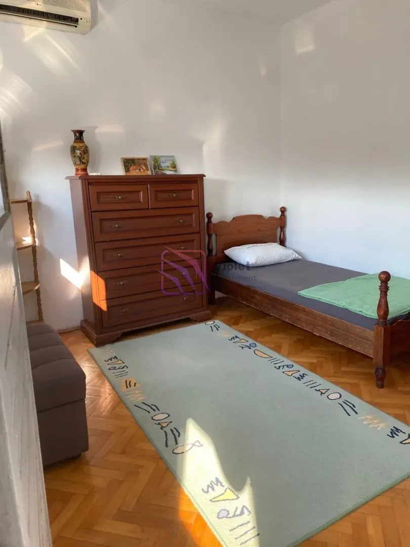Manja spavaća soba sa drvenim krevetom, komodom i parketom na podu.