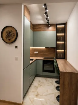 Modern kitchen with green fronts, wooden elements, and a breakfast bar with bar stools. - image 2