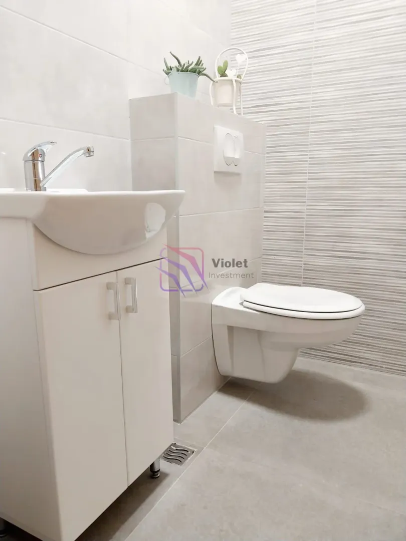 Small bathroom with a sink, vanity cabinet, and wall-hung toilet in neutral tones.